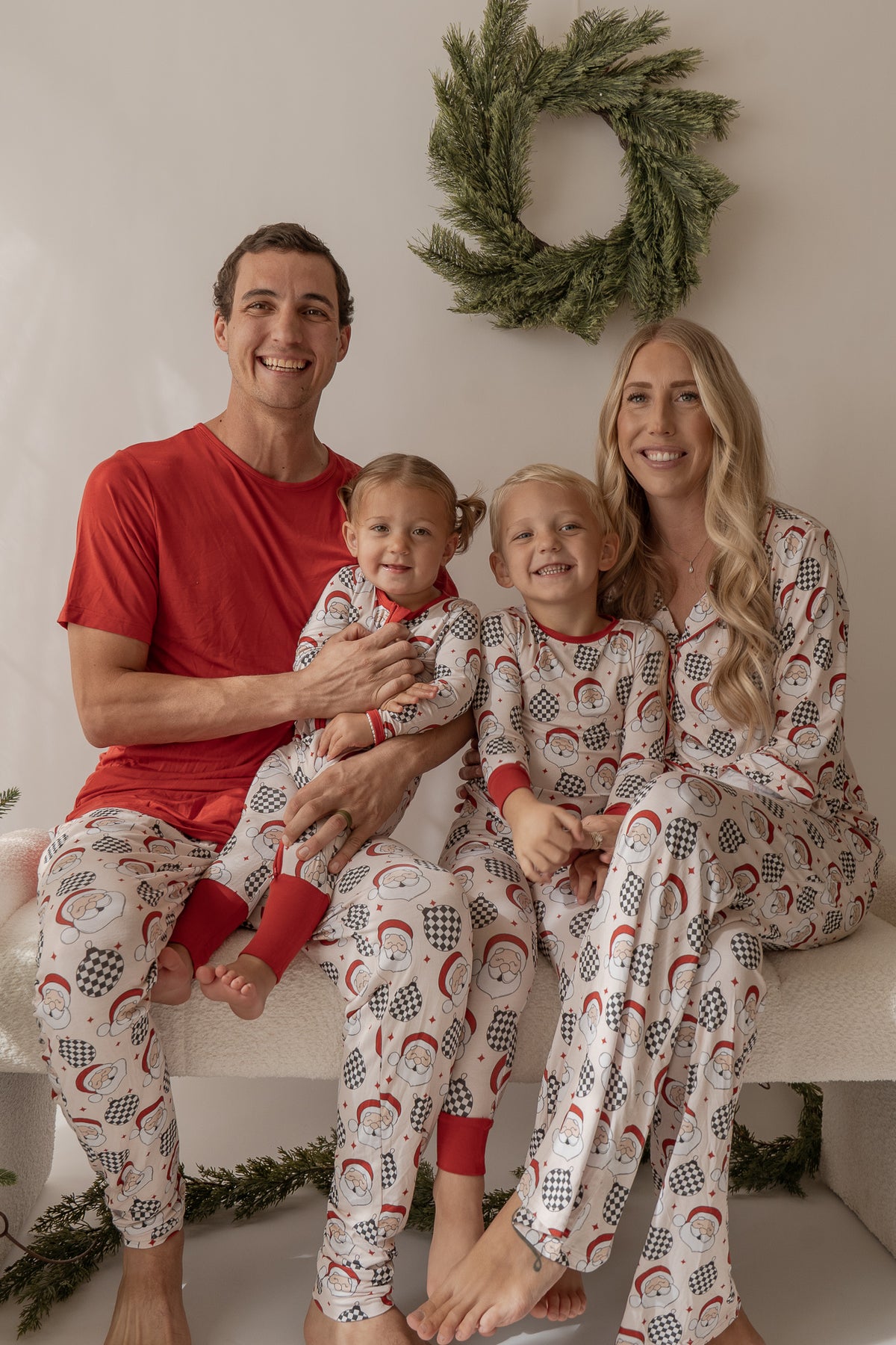 Family of four wearing matching pajamas in a festive setting with a wreath in the background.