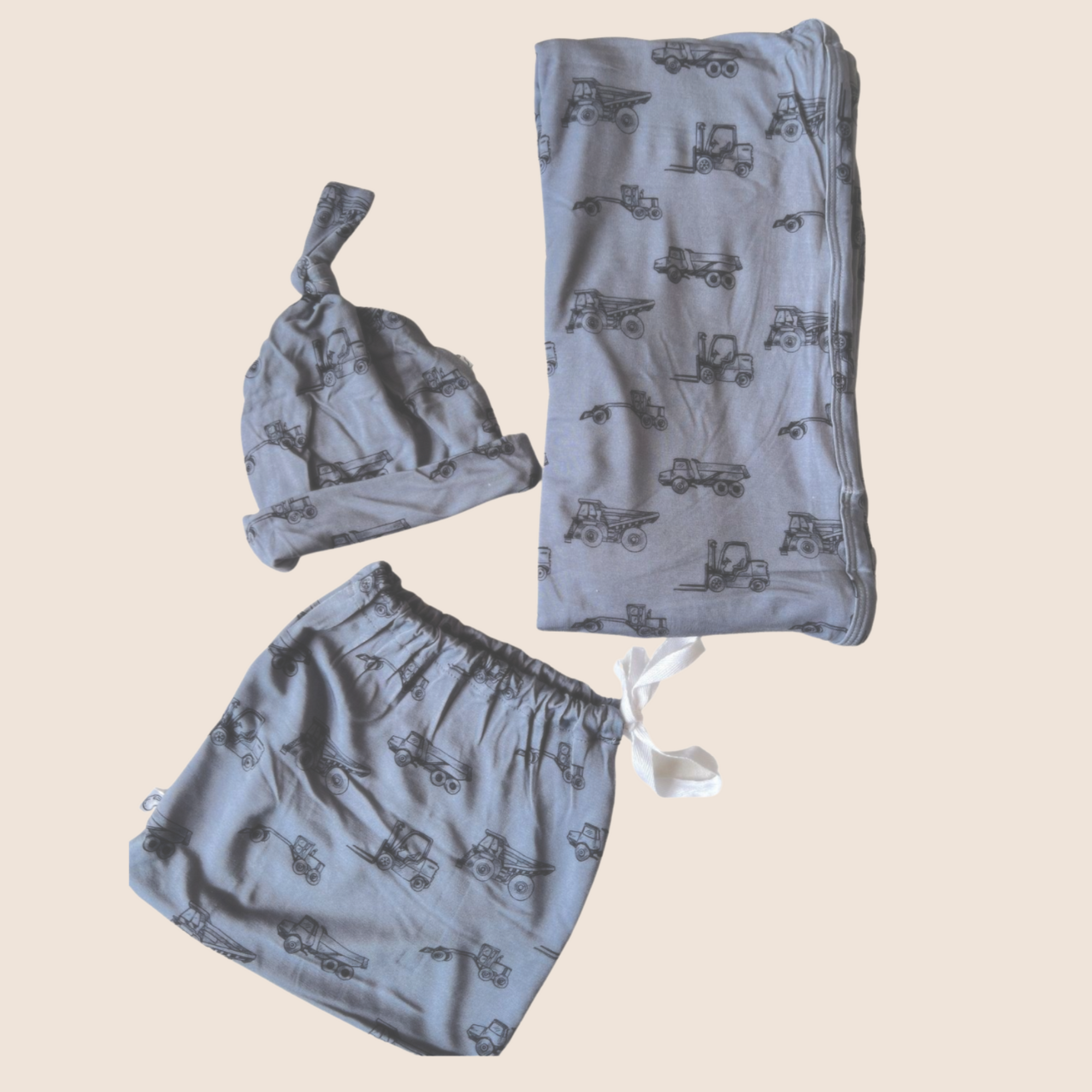 Newborn set with hat, blanket, and bag featuring truck patterns on a beige background.